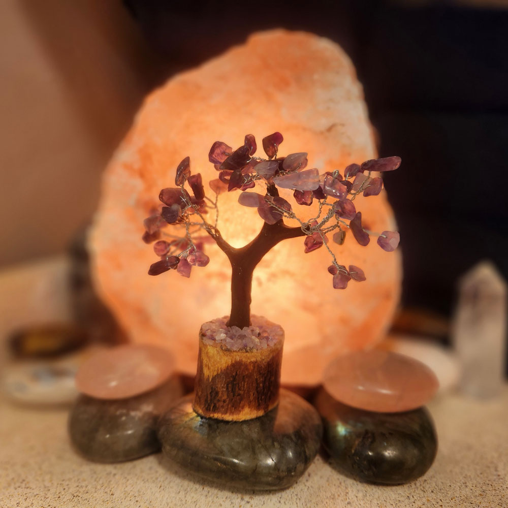 A small, decorative tree with purple gemstone leaves is placed in front of a glowing salt lamp, surrounded by polished stones, creating an ambiance similar to a serene spa in Ouray.