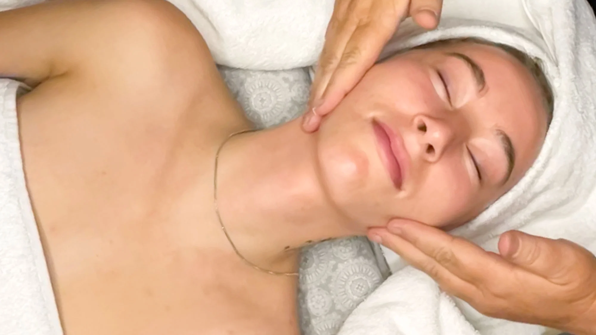 A person receives a relaxing face massage with eyes closed, resting on a cushioned surface covered in white towels, experiencing one of Ouray's rejuvenating facials.