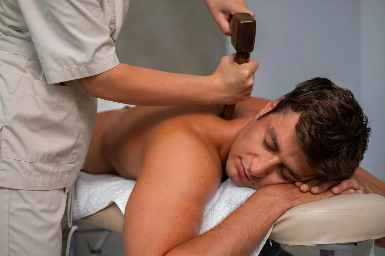 Man receiving a back massage with a wooden therapy tool.